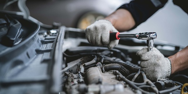 Close-up photo of a car mechanic working on a car engine in a mechanics repair service garage. A uniformed mechanic is working on a car service. Work in the garage, repair and maintenance services.