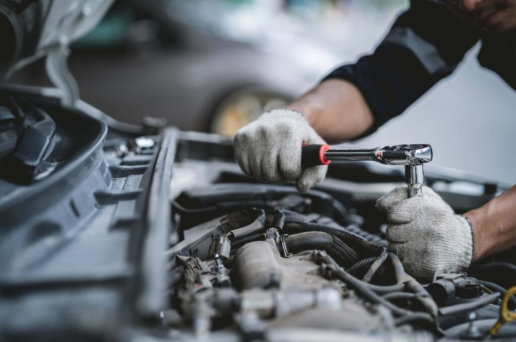 Close-up photo of a car mechanic working on a car engine in a mechanics repair service garage. A uniformed mechanic is working on a car service. Work in the garage, repair and maintenance services.